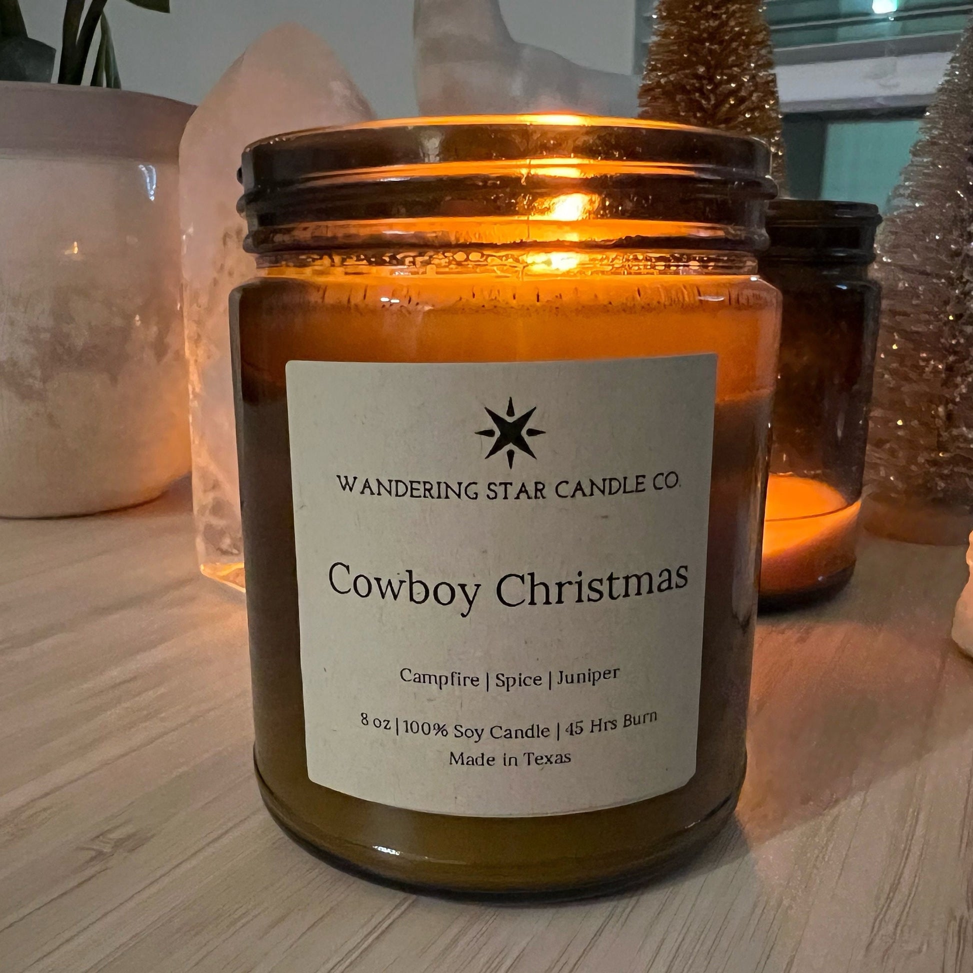 Photo of a lit amber jar candle featuring the scent of Cowboy Christmas, which is a blend of Campfire, Spice, and Juniper.