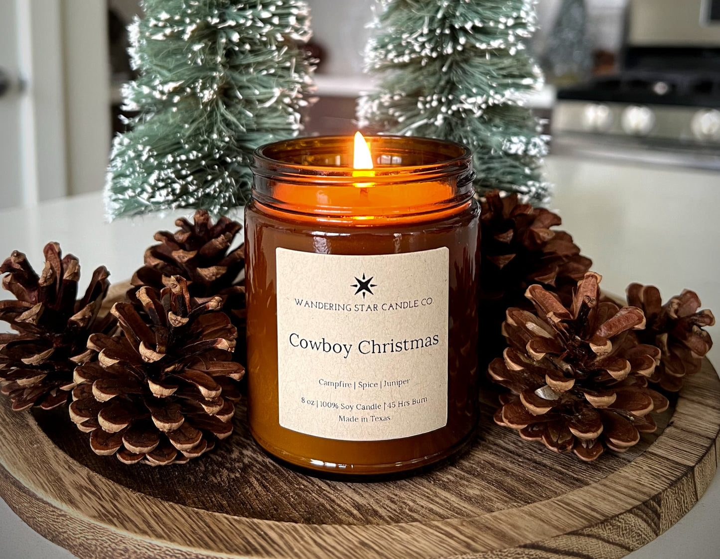 Photo of a lit amber jar candle featuring the scent of Cowboy Christmas, which is a blend of Campfire, Spice, and Juniper.